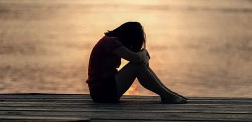 Woman sitting alone on dock by water, feeling lonely or contemplative.