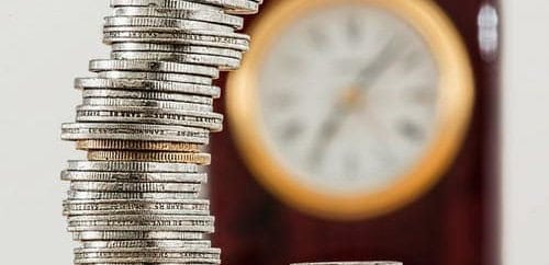 Stack of coins with a blurred clock in the background.