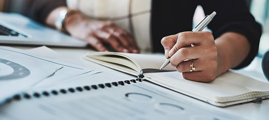 Person writing in a notebook during a business meeting at Trust Point.