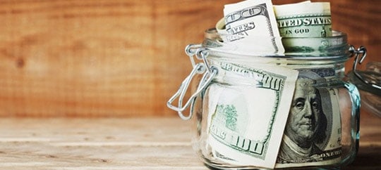 Glass jar filled with US dollar bills representing savings and investments.