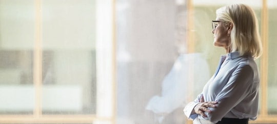 Businesswoman gazing out window, professional attire, modern office setting.