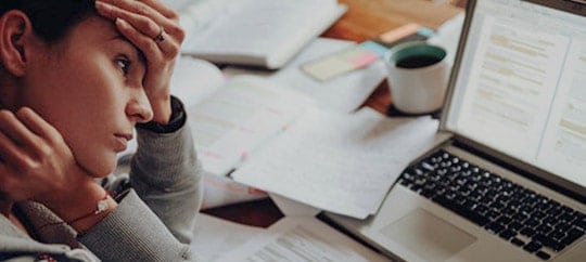 Woman stressed at work with laptop and papers on desk.