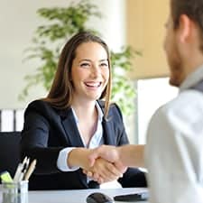 Businesswoman smiling and shaking hands with a client in an office setting.