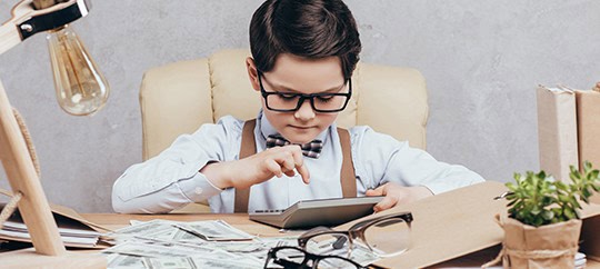 Child focused on tablet with books and glasses on desk.
