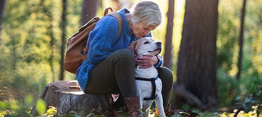 Senior woman hugging her dog in a forest setting for trust and companionship.