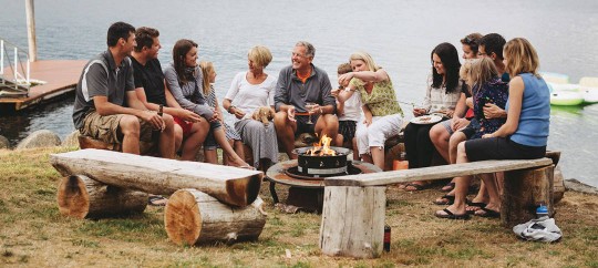large group of people at the lakeside with a fire pit