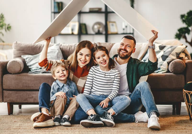 family sitting in front of couch with roof shaped wood piece held above head