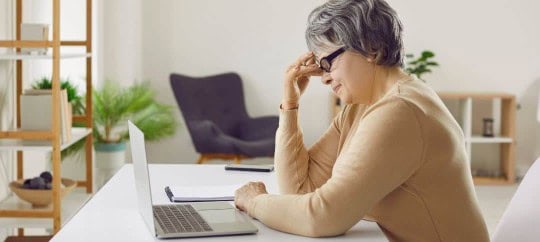 Woman working on laptop at home, stressed and worried.