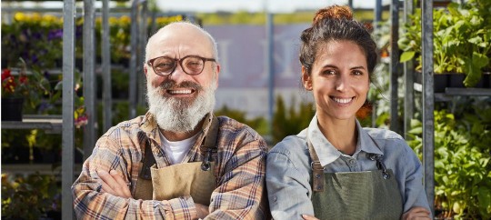 Two smiling entrepreneurs in a greenhouse, planning family business succession.