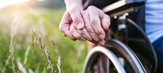 Person with hand on a wheel chair with a sunny and grassy background