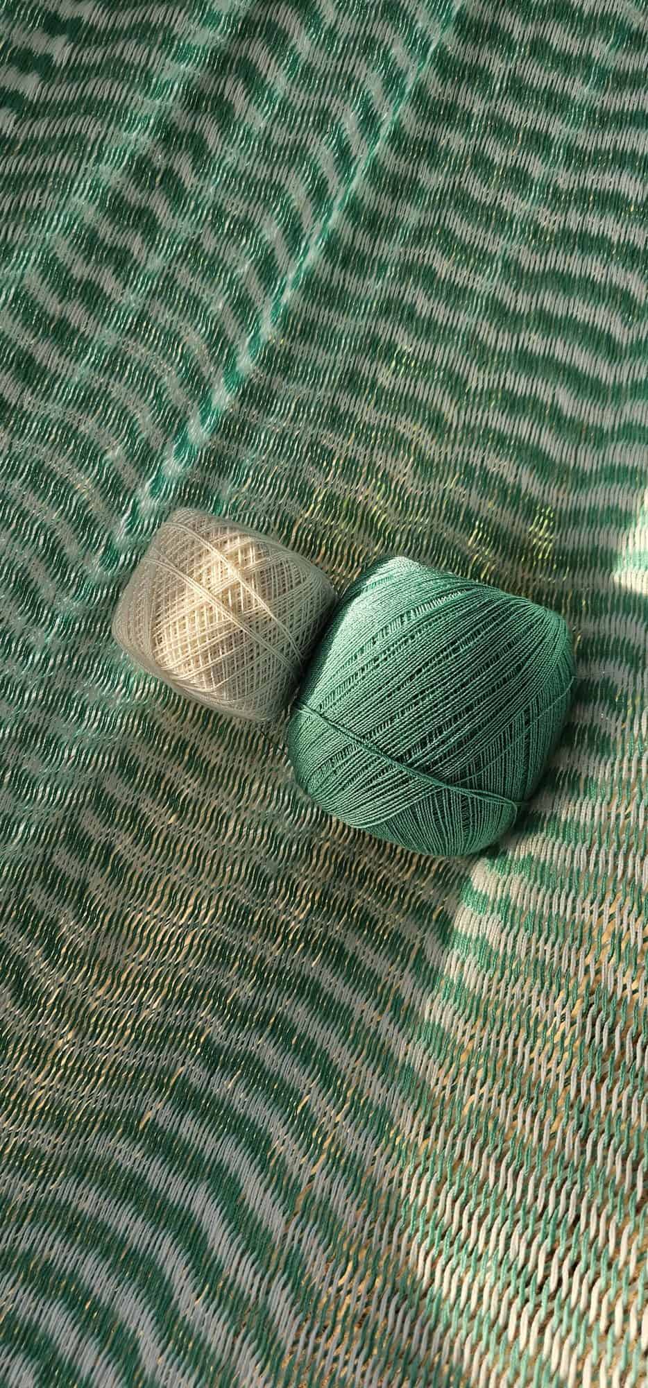 ULA "Mixcloud Mint" hammock in a mint green and white chevron pattern, with white ropes, relaxing on a sandy, treed beach or tropical park area.