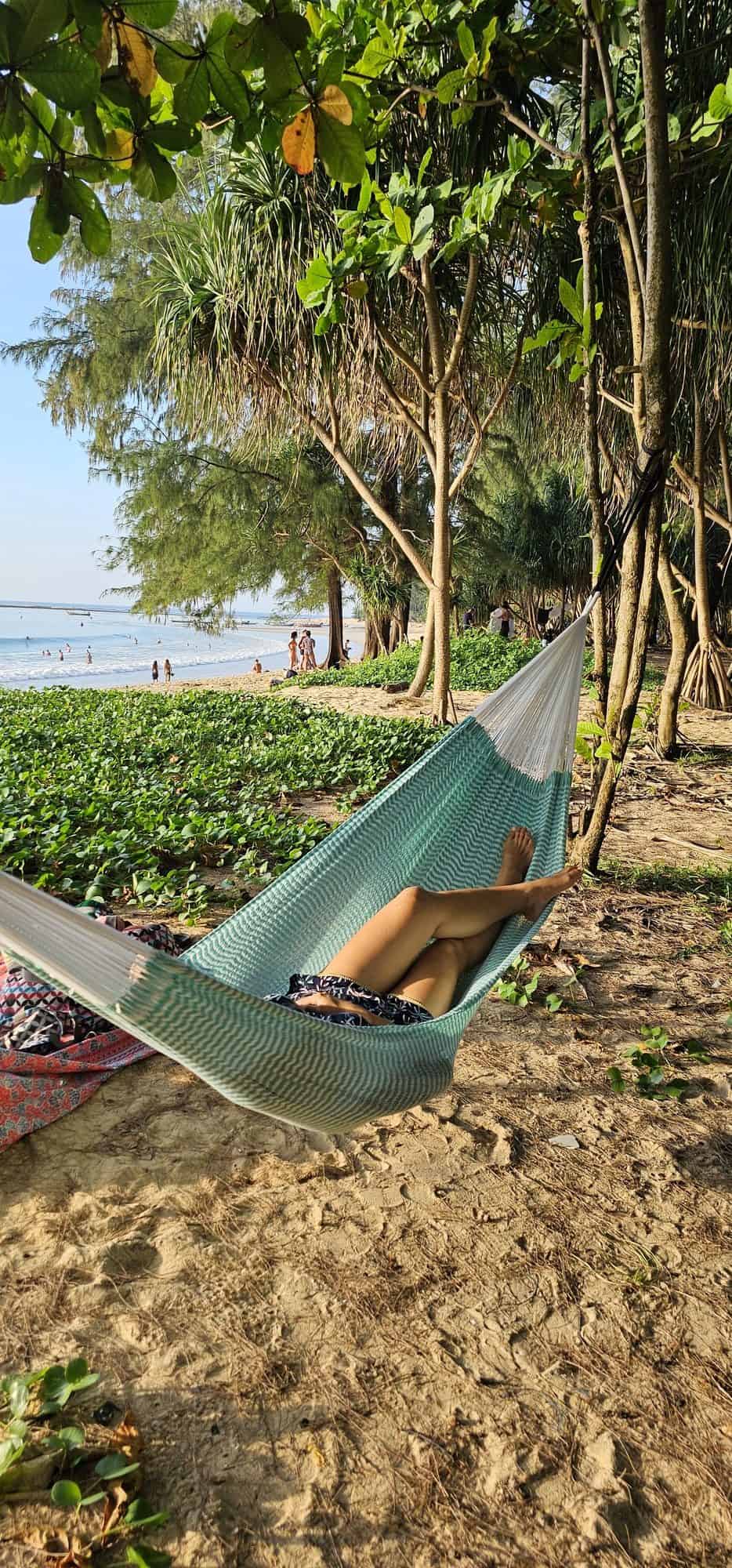 ULA "Mixcloud Mint" hammock in a mint green and white chevron pattern, with white ropes, relaxing on a sandy, treed beach or tropical park area.