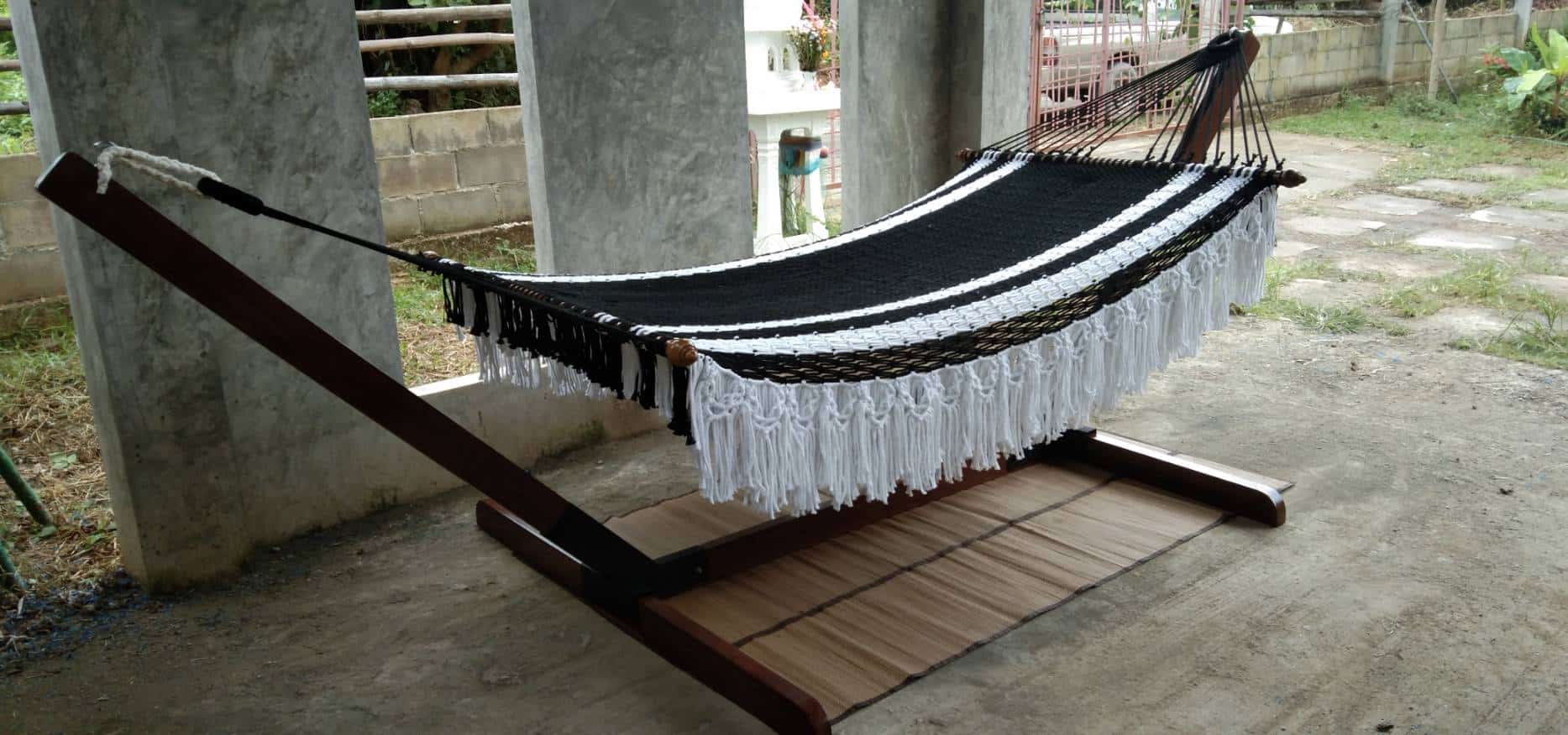 Outdoor black and white striped macrame hammock with fringe on a heavy duty wood stand.