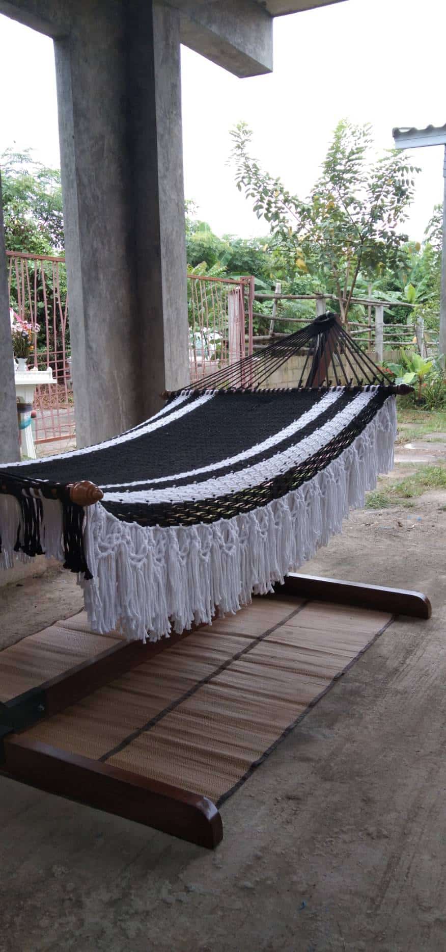 Outdoor black and white striped macrame hammock with fringe on a heavy duty wood stand.