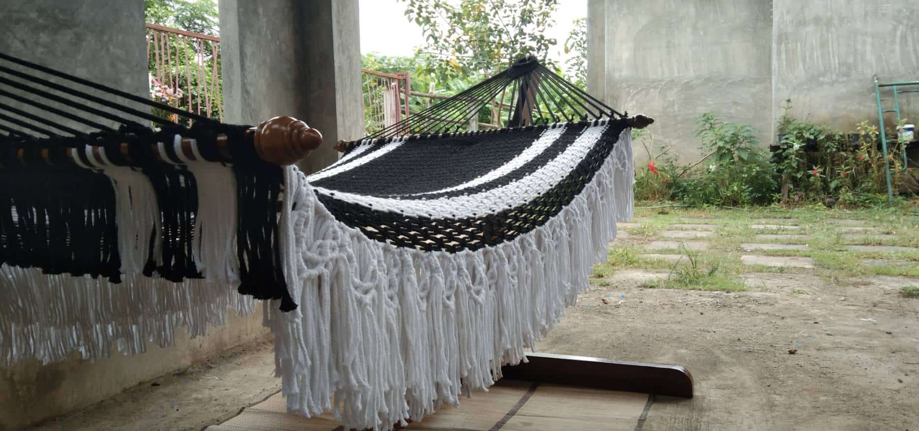Outdoor black and white striped macrame hammock with fringe on a heavy duty wood stand.