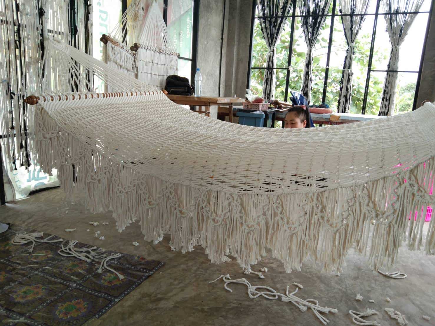 Large white rope hammock with fringe and wooden spreader bars in a macrame workshop.