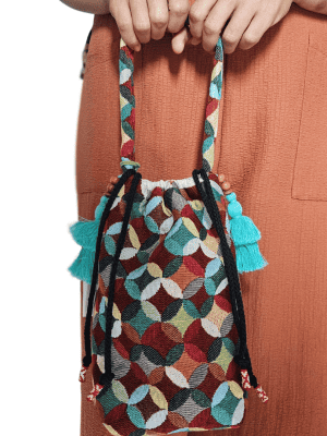A stylish drawstring bucket bag or pouch bag featuring a vibrant, multi-color geometric fabric pattern with interlocking circle or Seigaiha wave motifs with bohemian style. The textile includes shades of teal, burgundy, olive green, cream, and brown. Decorated with tassels and wood beats