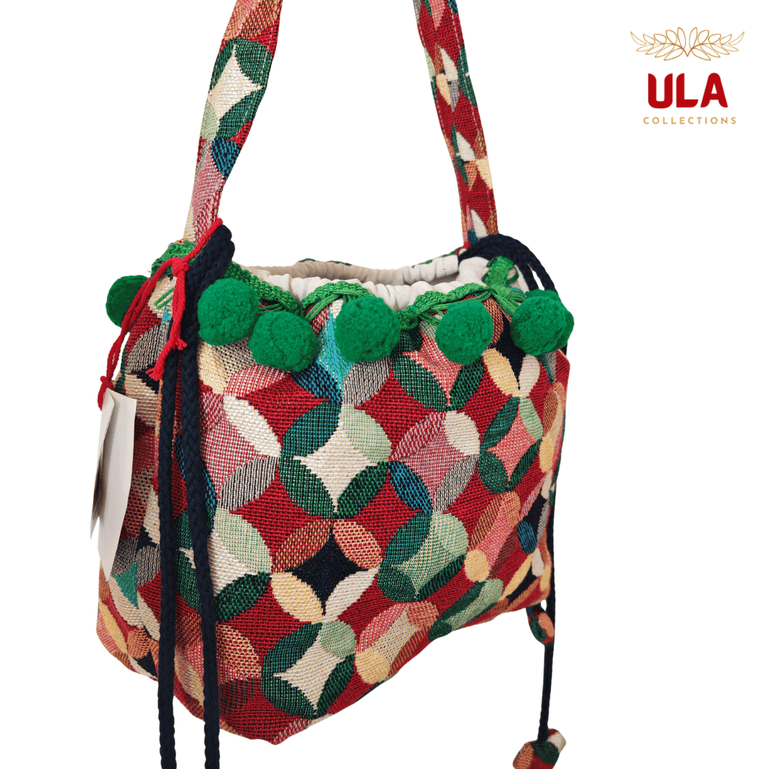 handmade woven drawstring bucket bag with a colorful patchwork/circle pattern in red, green, and cream, featuring dark green pom-poms.