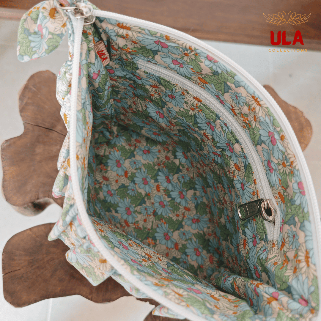 Detailed close-up of a white zipper and a light blue floral fabric bow on a blue canvas pouch with matching ruffled accents.