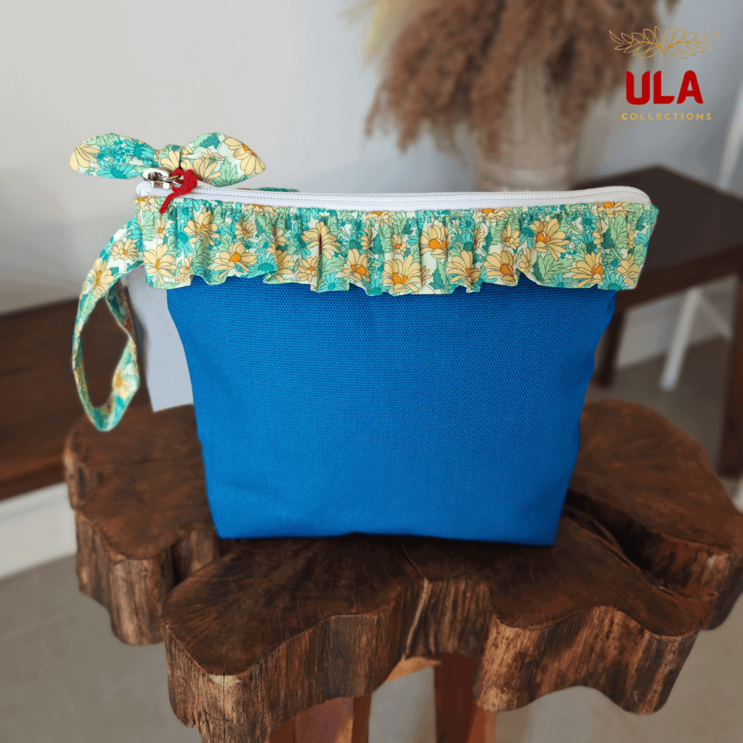 Exterior of a bright blue canvas pouch featuring a green and yellow floral ruffled trim and a matching fabric bow charm on the zipper.
