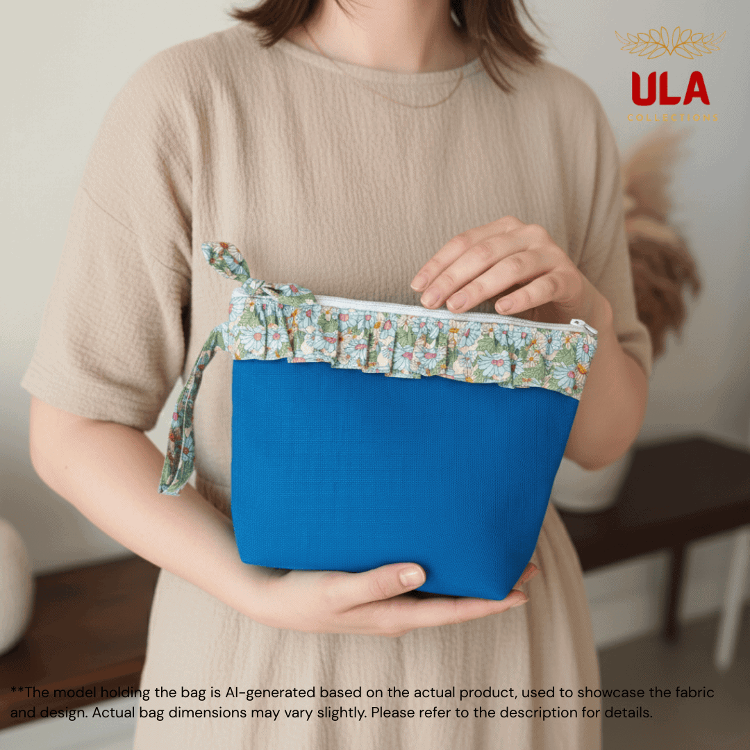 An AI-generated lifestyle image featuring a model in a neutral-toned dress holding a royal blue canvas pouch. This version of the bag has a pale green and blue floral ruffle trim and a matching wristlet strap. The model’s hands are shown resting on the bag to demonstrate its size and scale. A disclaimer at the bottom notes that the model is AI-generated to showcase the design.