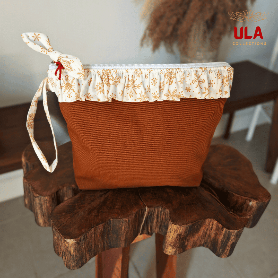 A handcrafted brown canvas pouch featuring a white ruffled top edge with a gold snowflake pattern, displayed on a rustic wooden pedestal.