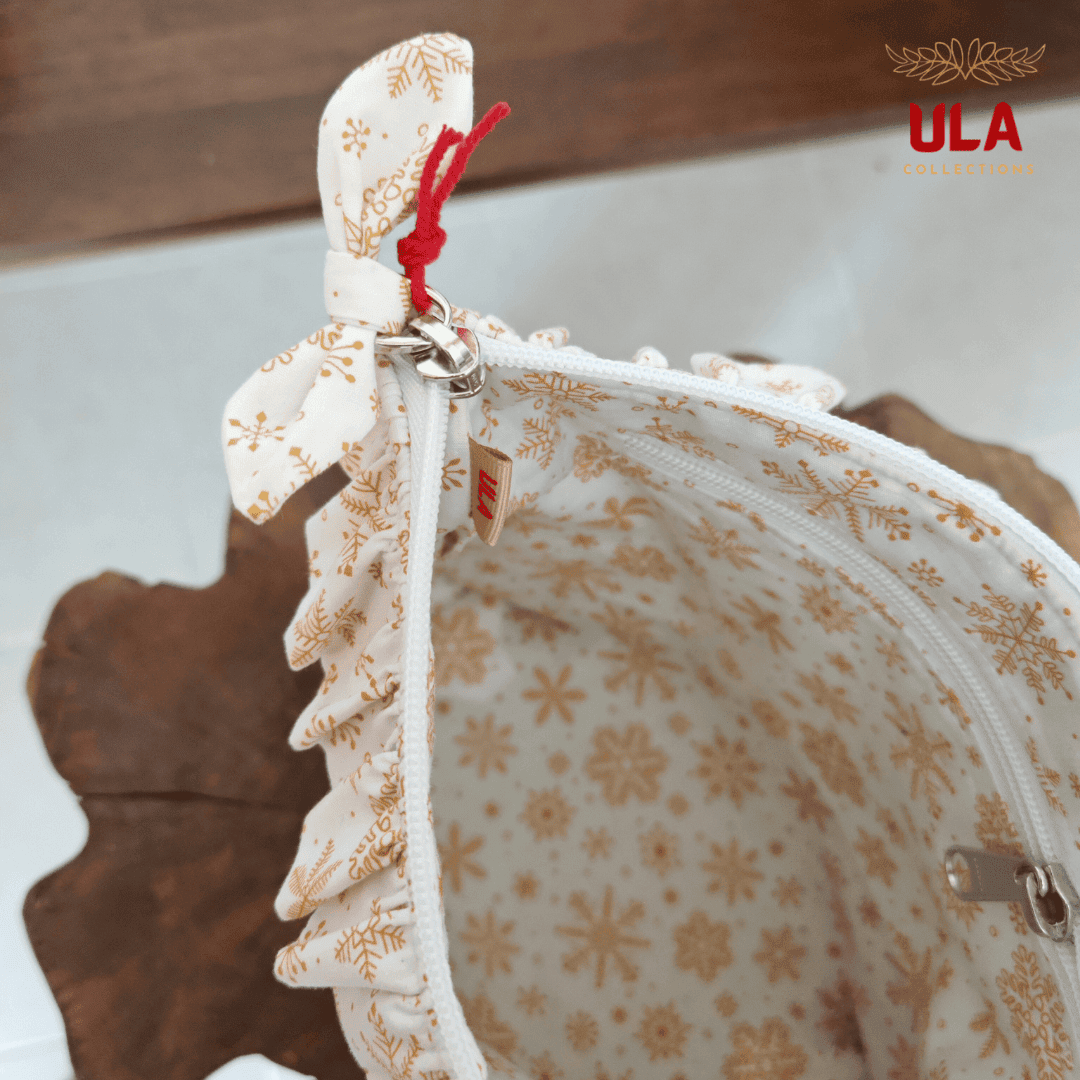 Close-up of a zippered cosmetic bag showing a white snowflake patterned lining, and a small ULA Collections brand tag.