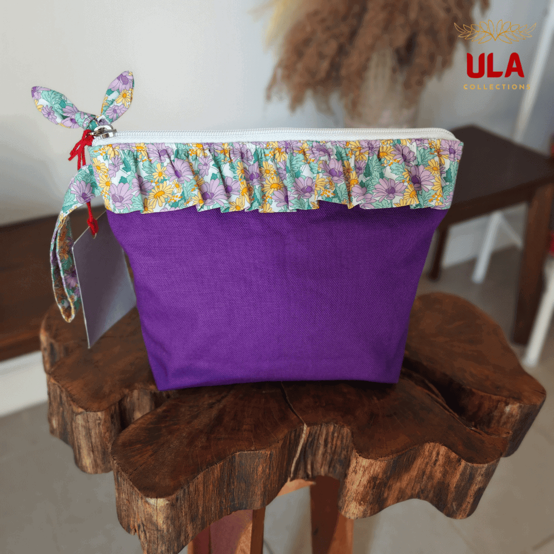 Front view of a deep purple canvas bag by ULA Collections with a purple, yellow, and green floral ruffled trim and bow detail.