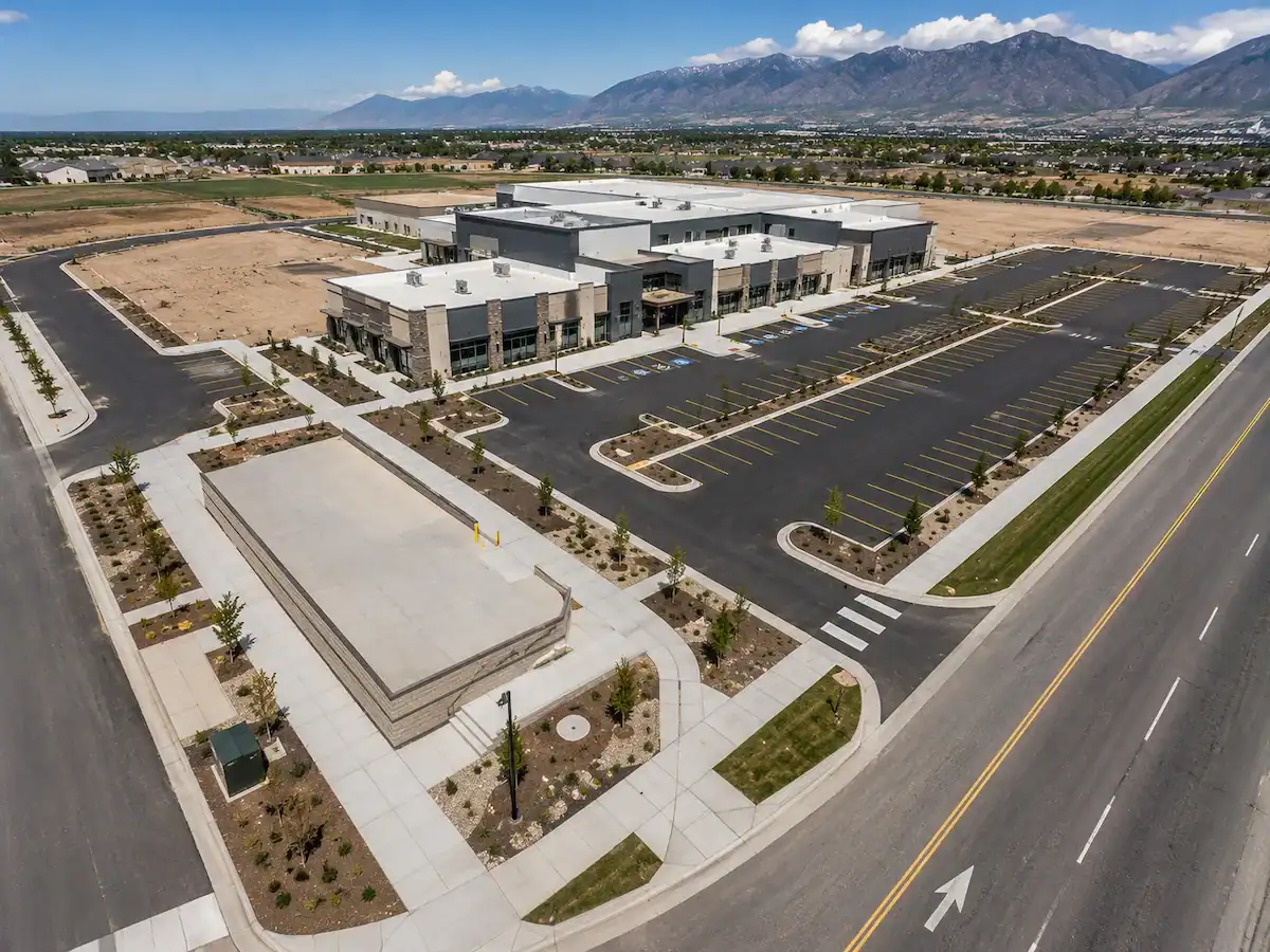 Aerial view of a commercial development in Utah featuring concrete sidewalks, curbs, building pads, and fresh asphalt parking lots.