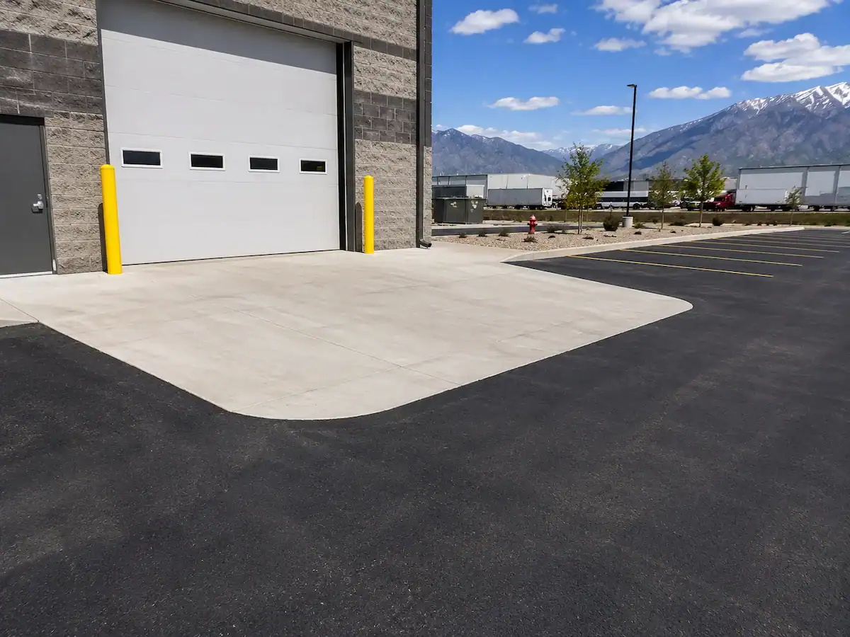 Concrete loading apron transitioning into a freshly paved asphalt parking lot at a commercial property in Utah.