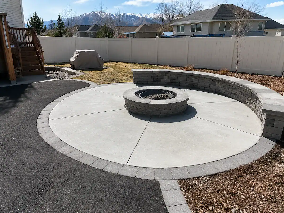 Residential backyard in Utah featuring a concrete fire pit patio and asphalt walkway with mountain views.
