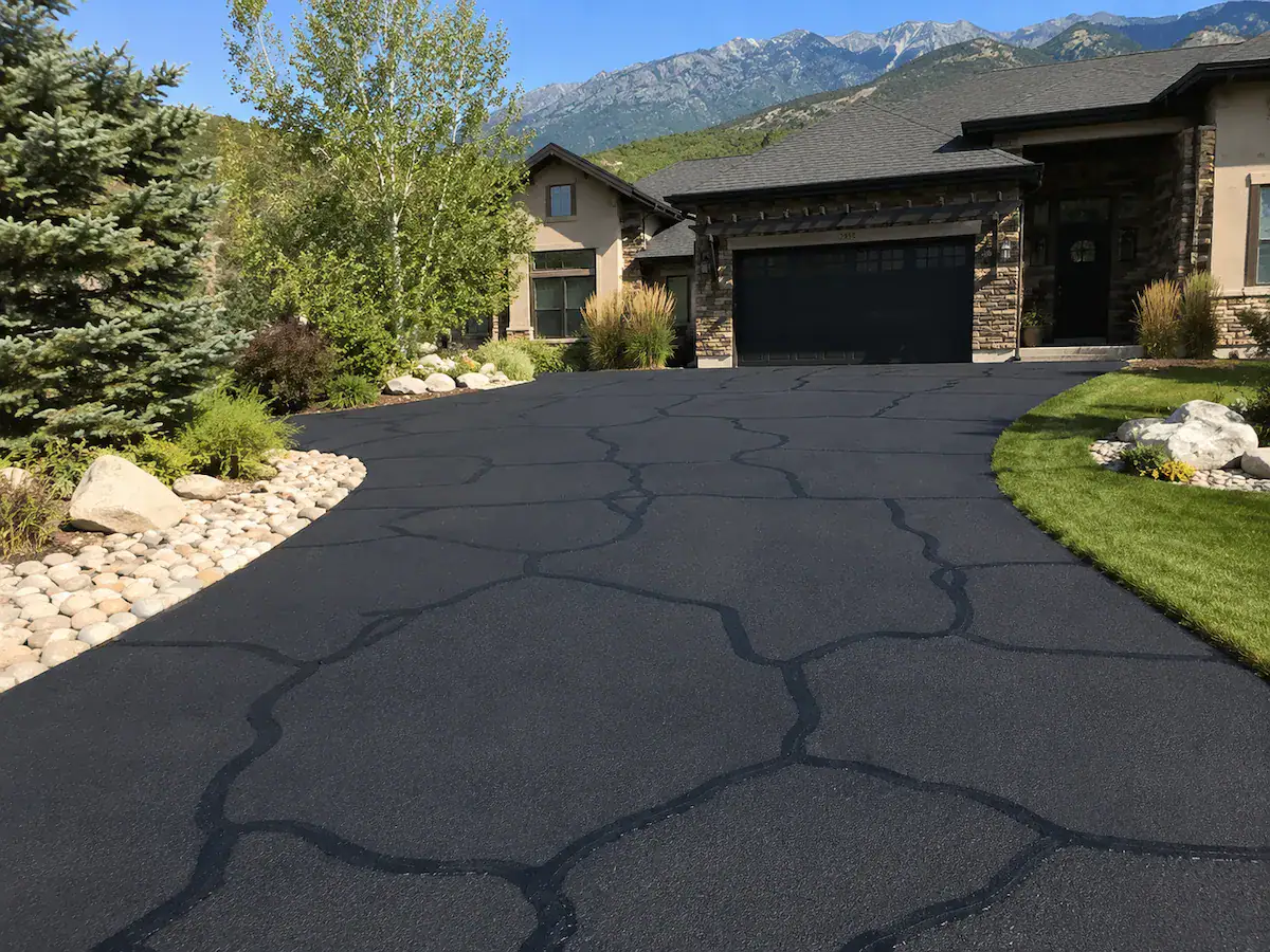 Residential asphalt driveway in Utah with freshly sealed cracks and mountain backdrop