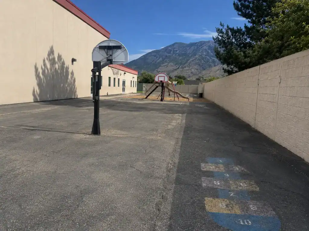 Before photo of faded basketball court markings on weathered asphalt at Timpanogos Academy in Lindon, Utah before crack sealing, sealcoating, and restriping.
