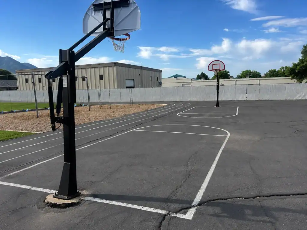 Before photo of weathered outdoor basketball court with faded game markings and worn asphalt at Timpanogos Academy in Lindon, Utah before sealcoating and restriping.