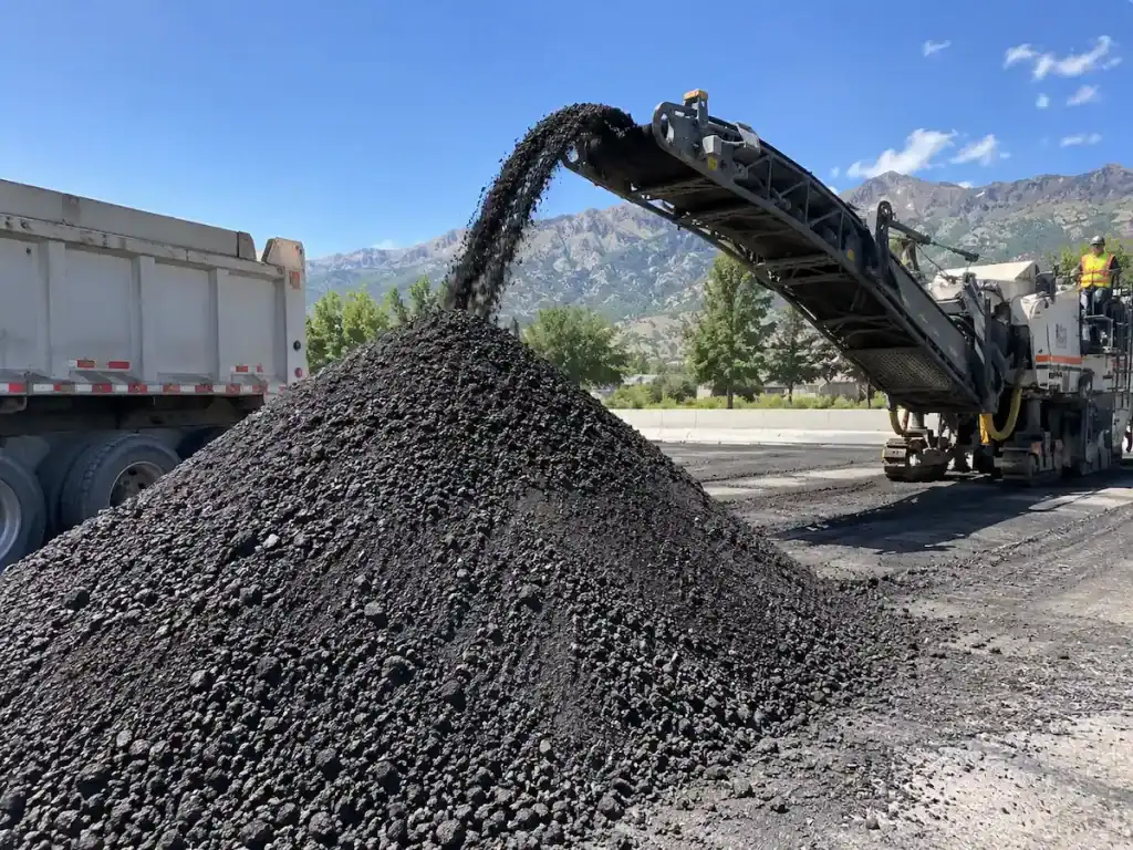 Asphalt millings being removed by a milling machine at a Utah paving project with mountains in the background.