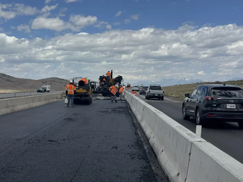 Eckles Paving crew installing and compacting new asphalt along I-15 in Mona, Utah, with traffic moving beside the construction zone.