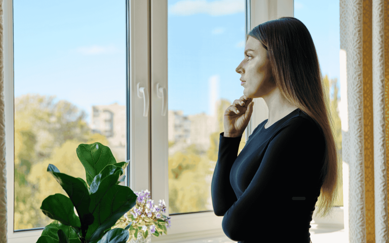Woman looking out a window in quiet reflection, representing the experience of late diagnosed ADHD in women