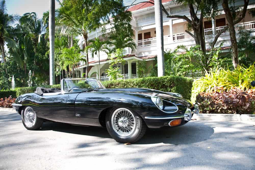 Classic vintage Jaguar parked outside a home with palm trees