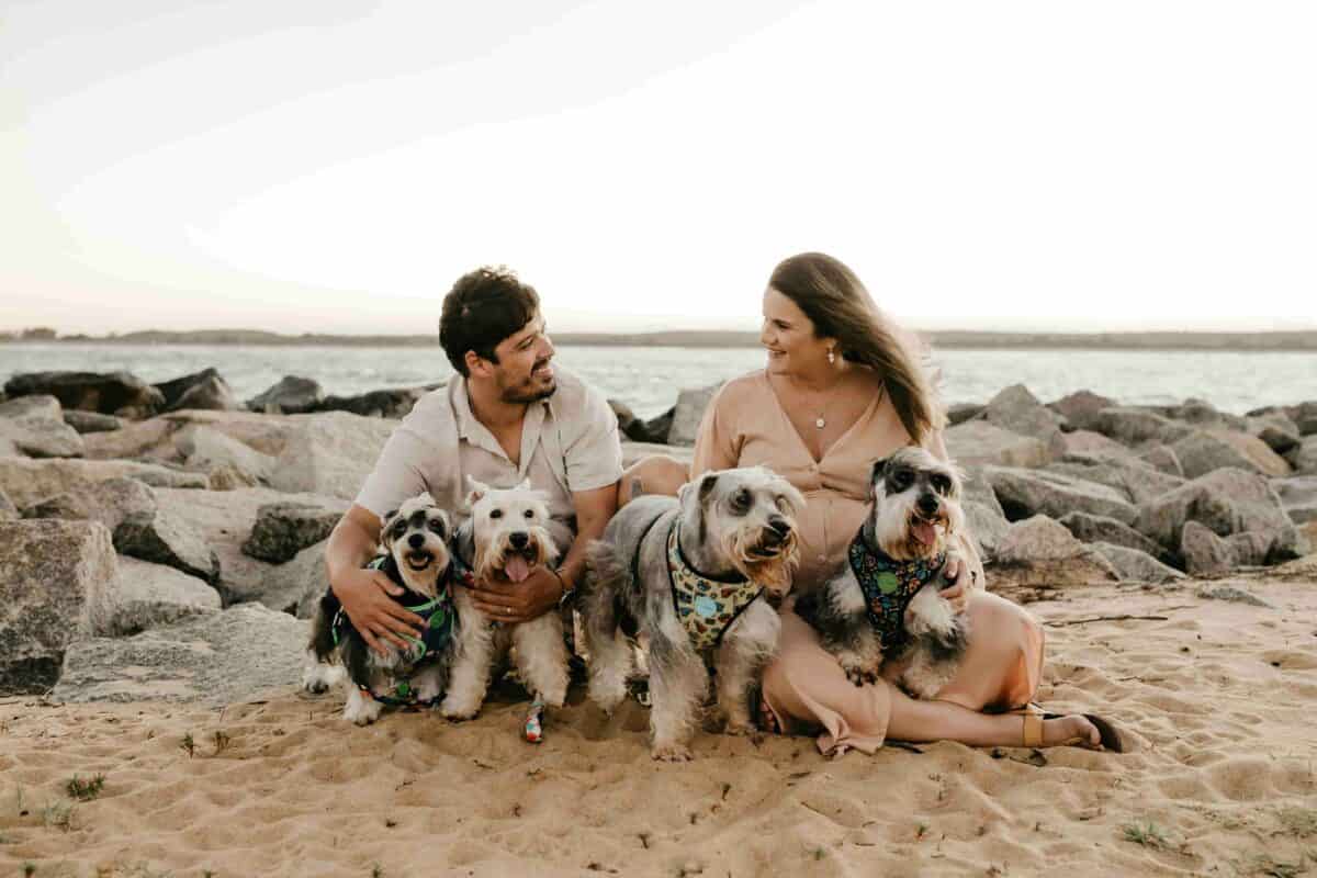 Happy couple with 4 dogs on the beach, symbolizing a joyful reunion after pet relocation to Puerto Rico.