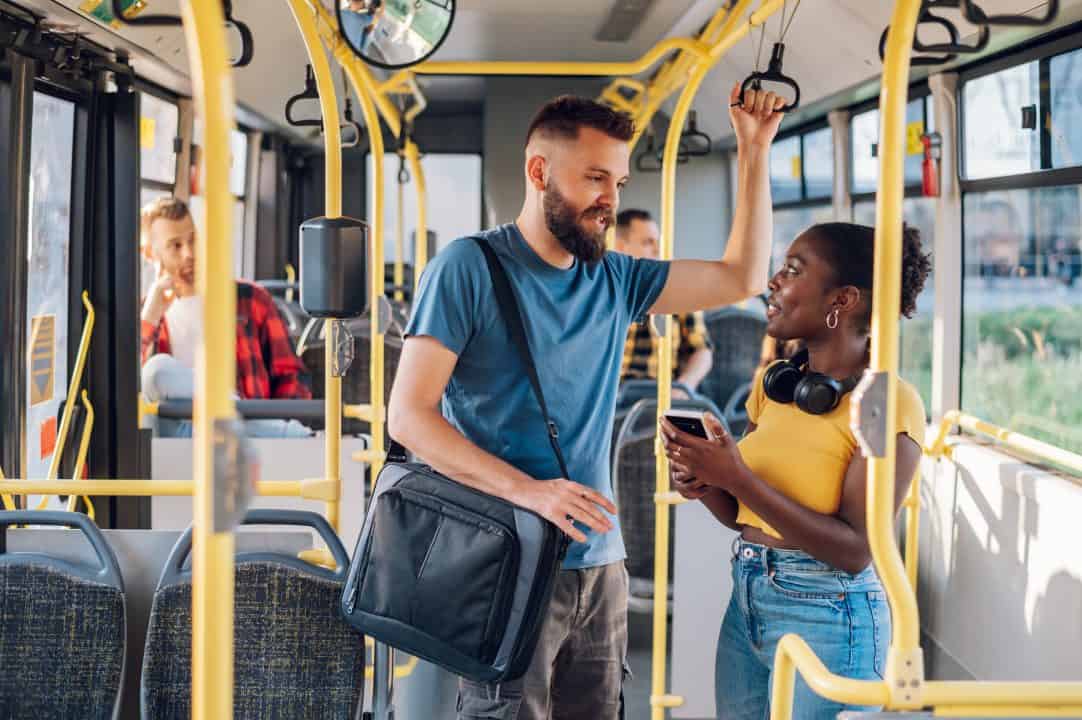 Two people are standing on a bus conversing while in a good mood.