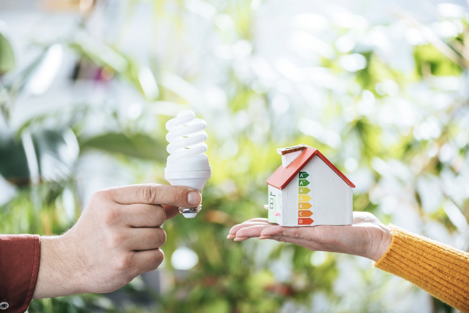 Energy Efficiency through new lightbulbs and house on peoples palms with green background