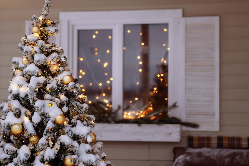 A Snow Covered Christmas Tree Decorated With Holiday Lights with more white christmas lights in background of suburban Minnesota house