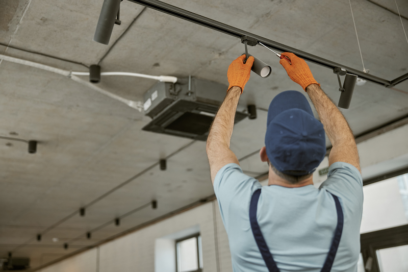 Male Electrician Fixing Flickering Lights On Ceiling Lamp In Building