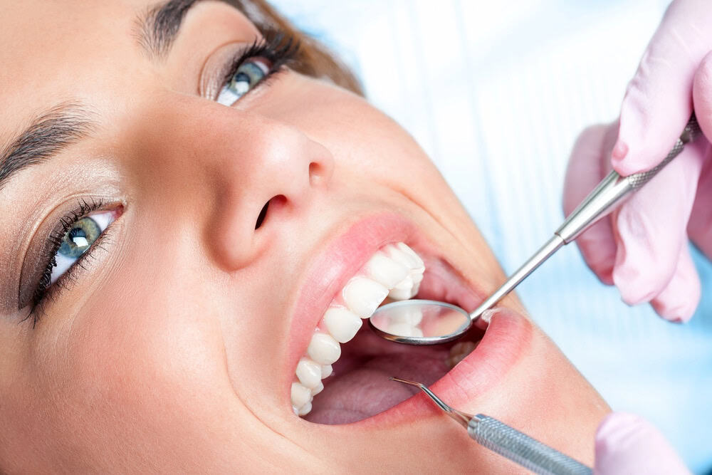 close up of woman during dental cleaning with dental mirror and scraper in her mouth