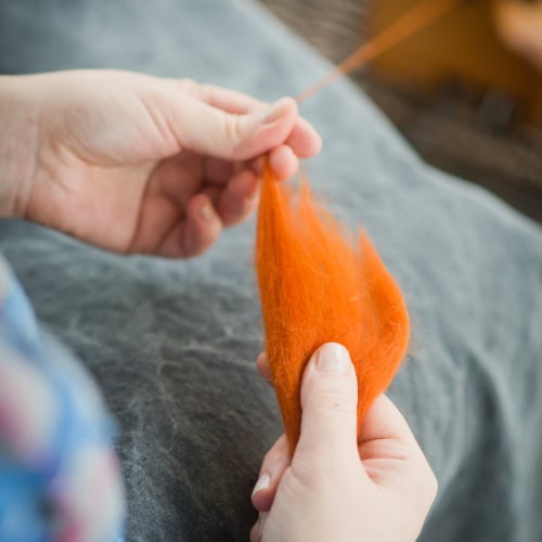 Two hands are holding orange wool fiber and drafting the combed top to spin into yarn