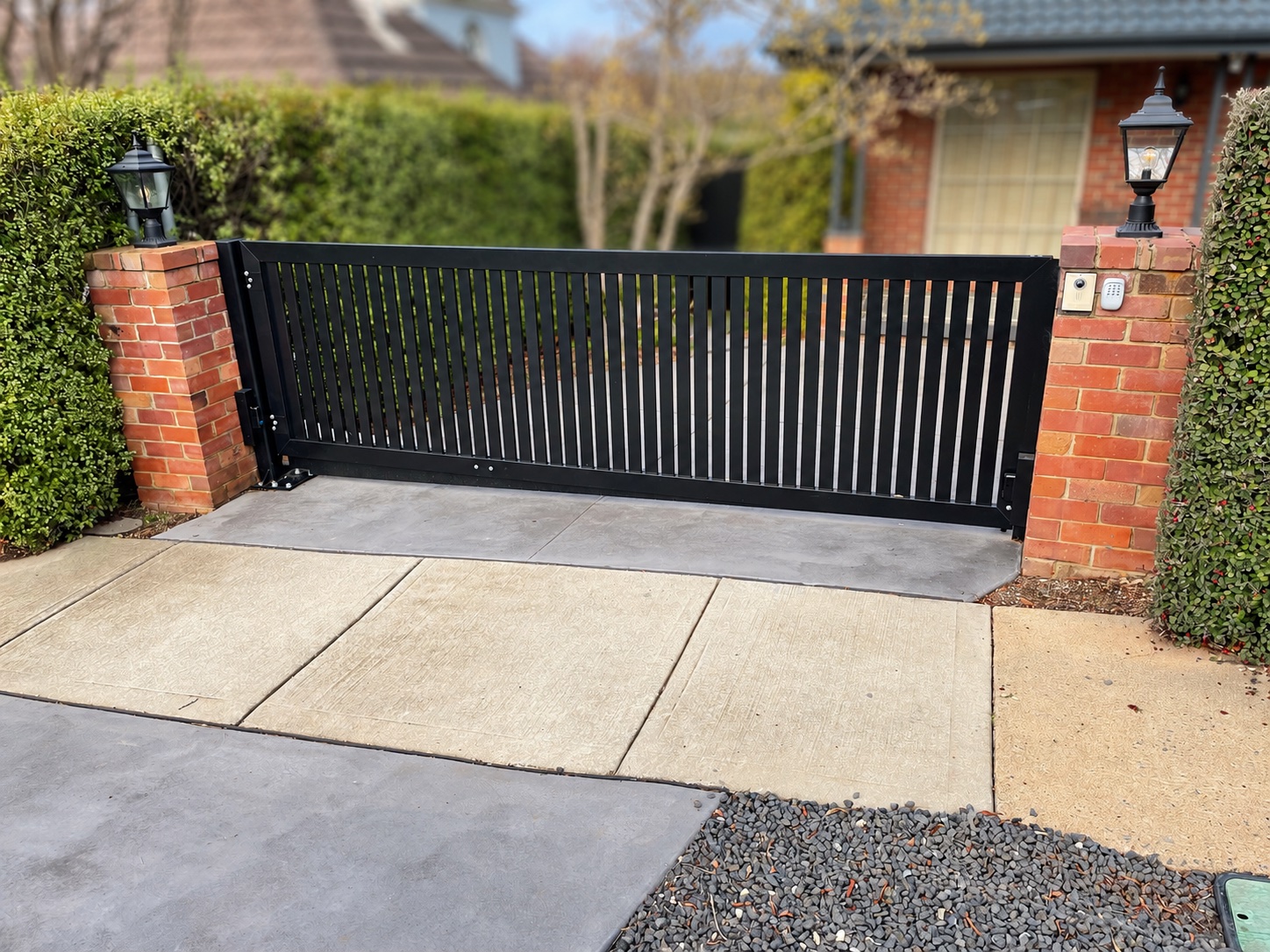 Black vertical-slat driveway gate between brick pillars
