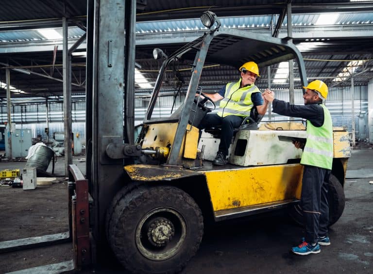 Two men are standing next to a forklift, one of them is wearing a yellow vest. Scene is serious and focused, as the men are likely discussing or inspecting the forklift
