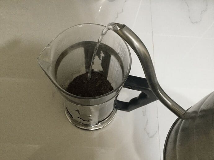 Pouring hot water into the French Press over coffee grounds 