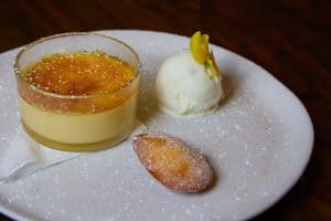 Creamy custard dessert with caramel topping, accompanied by vanilla ice cream and a delicate biscuit on a white plate.