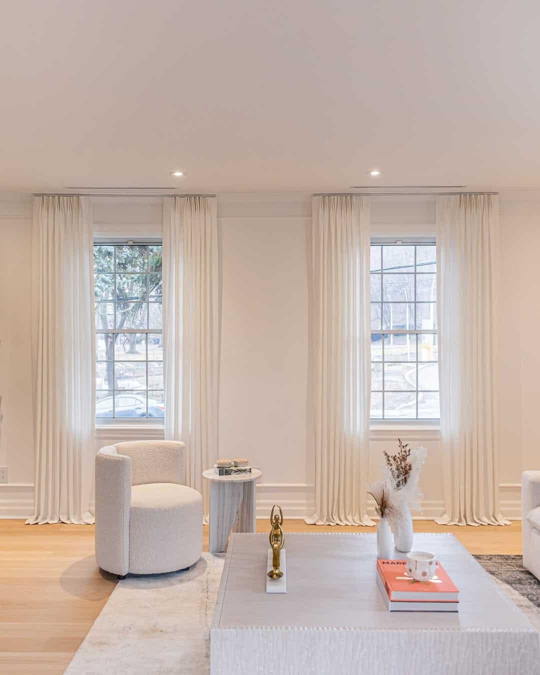 Bright living room, large windows, white curtains, cozy seating, stylish decor.